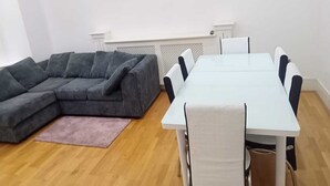 A living room with a grey sectional sofa, a white dining table with six chairs, a pink rug, and a white radiator. - Charming 2-bed Apartment in Wolverhampton (Wolverhampton)