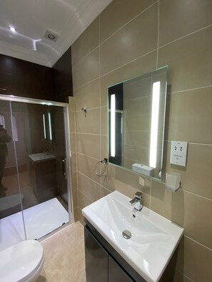A modern bathroom with a glass shower enclosure, a white sink, and a large mirror. - Charming 2-bed Apartment in Wolverhampton (Wolverhampton)