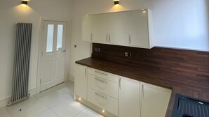 A modern kitchen with white cabinets, a wooden countertop, and recessed ceiling lighting. - Charming 2-bed Apartment in Wolverhampton (Wolverhampton)