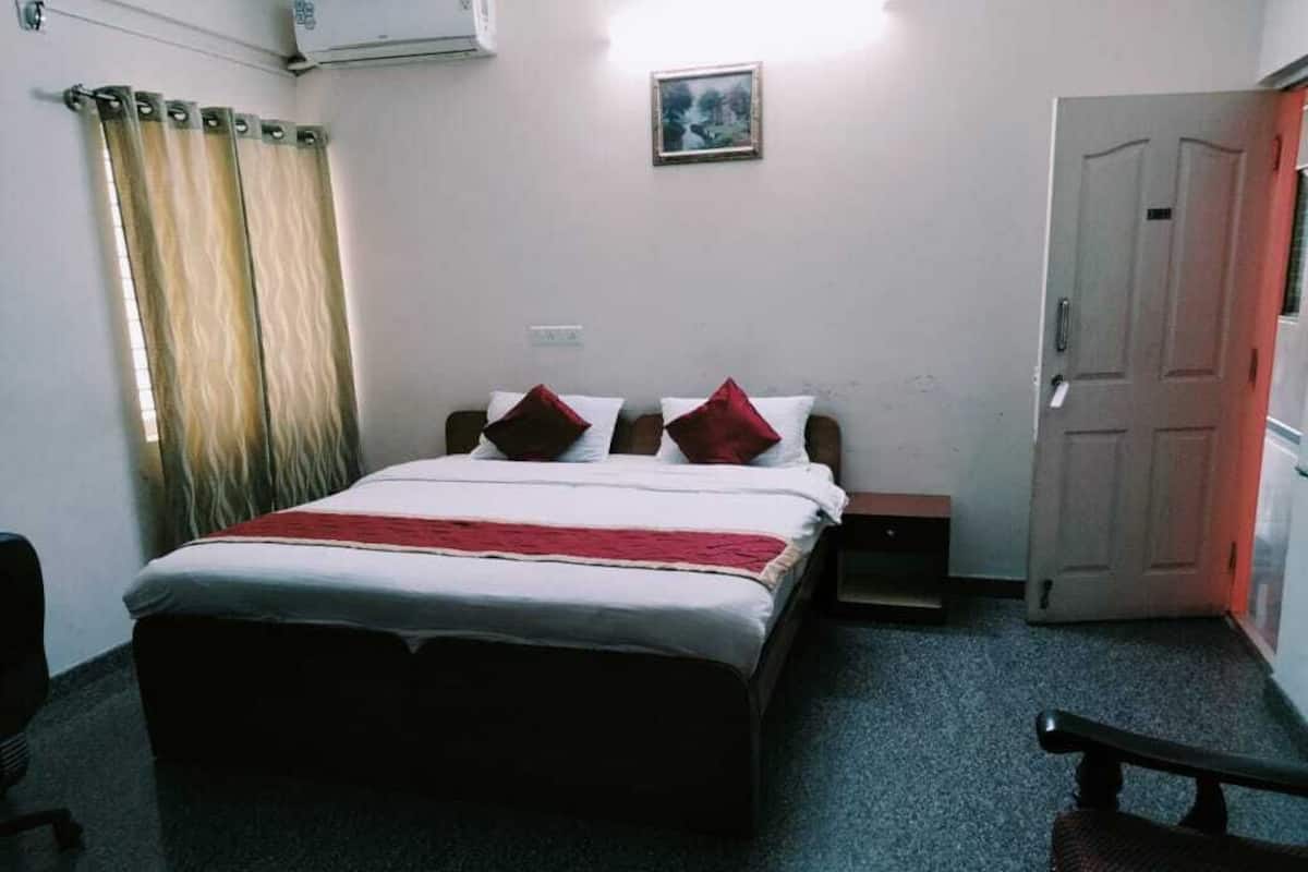 Een slaapkamer met een bed, een nachtkastje, een stoel, een deur en een raam met gordijnen.