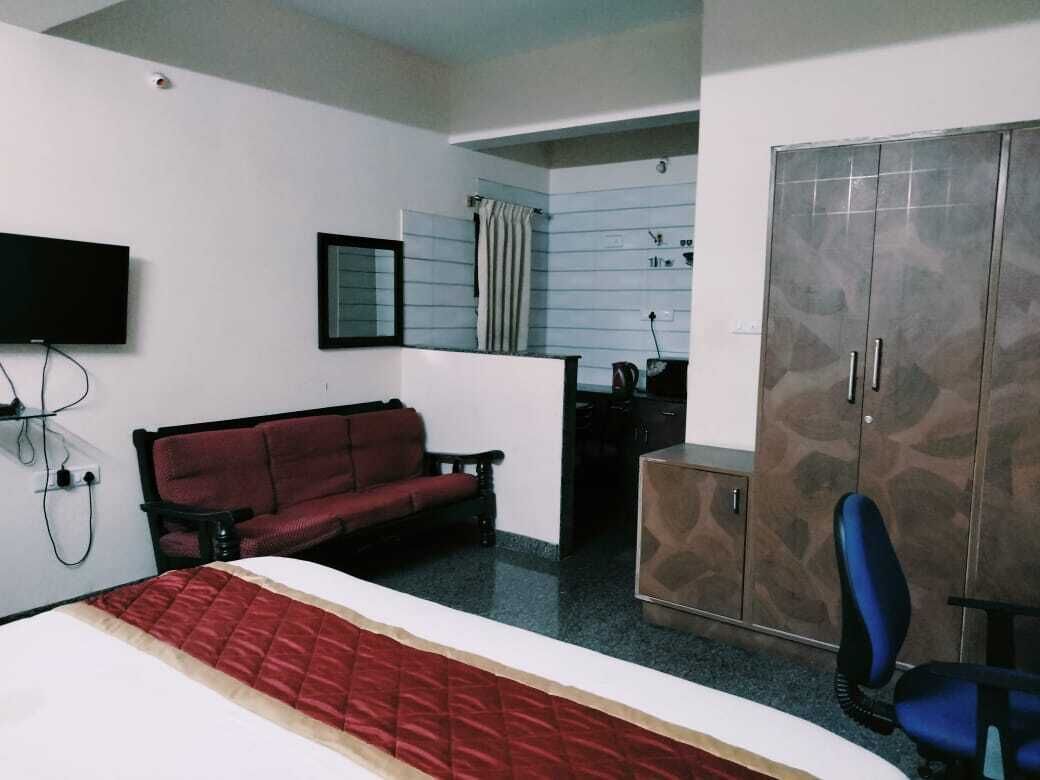 A hotel room with a bed, a red sofa, a desk with a chair, a wardrobe, and a television mounted on the wall.
