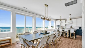 Un comedor amplio con una mesa grande y sillas de mimbre, con vistas a un paisaje marino.