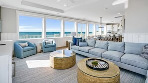 Un salón espacioso con un sofá grande, dos sillones y una mesa de centro. La habitación tiene ventanas amplias que ofrecen vistas al océano.
