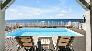 Zona de piscina con vista al océano, terraza de madera y barandillas blancas.