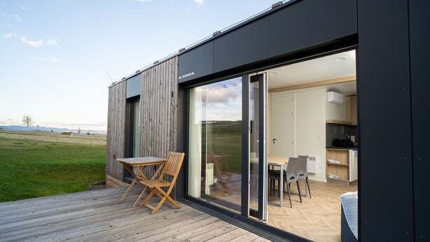 A modern house with a wooden deck, a dining area with chairs, and a kitchen visible through glass doors. - Royal Village (Malý Slavkov)