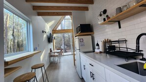 A modern kitchen with wooden beams, white cabinets, a large window, and a view of the outdoors. - Luxury Cabin - Riolago (Montgomery County)