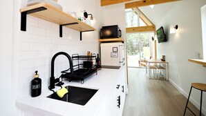 Une cuisine moderne avec des carreaux blancs, des poutres en bois, un évier noir et un coin repas comprenant une table et des chaises.