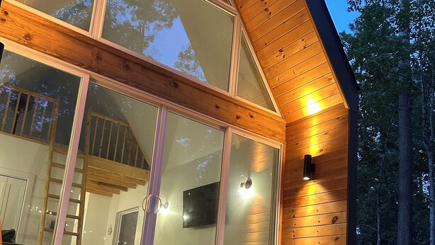 Une cabane moderne en bois, dotée de grandes portes vitrées, d’un bain à remous et d’une terrasse en bois.