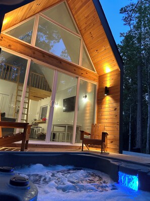 Una cabaña moderna de madera con grandes puertas de vidrio, un jacuzzi y una terraza de madera.
