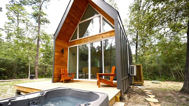 Una cabaña de madera moderna con jacuzzi, terraza de madera y puertas de cristal que dan a un patio.