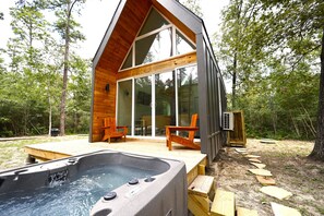 Una cabaña de madera moderna con jacuzzi, terraza de madera y puertas de cristal que dan a un patio.