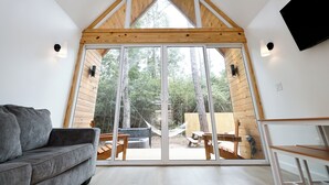 Un interior moderno con techo inclinado, amplios ventanales que dan a un espacio exterior, un sofá gris y muebles de madera.