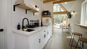 Eine moderne Küche mit weißen Schränken, einer schwarzen Spüle und Holzbalken an der Decke. Durch einen offenen Durchgang ist ein Essbereich mit Tisch und Stühlen zu sehen.