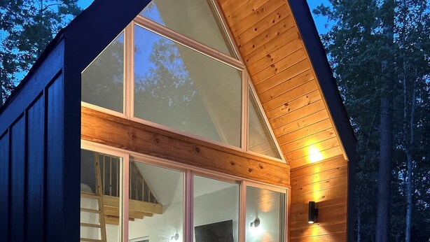 Eine moderne Holzhütte mit Whirlpool, einer Holzdiele und großen Glasschiebetüren zu einem Innenraum mit Fernseher und Sitzgelegenheit.