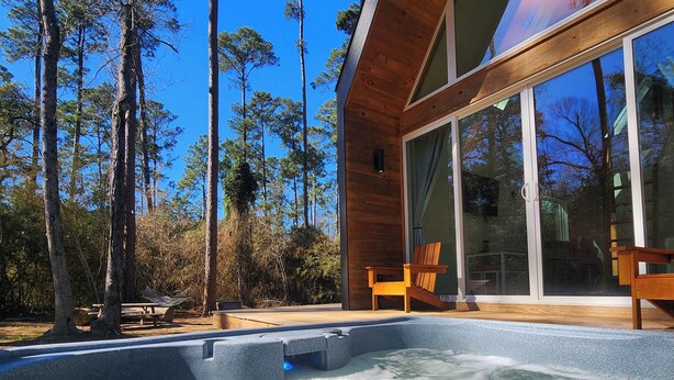 Un jacuzzi con cubierta de madera y paredes de vidrio, rodeado de árboles altos.