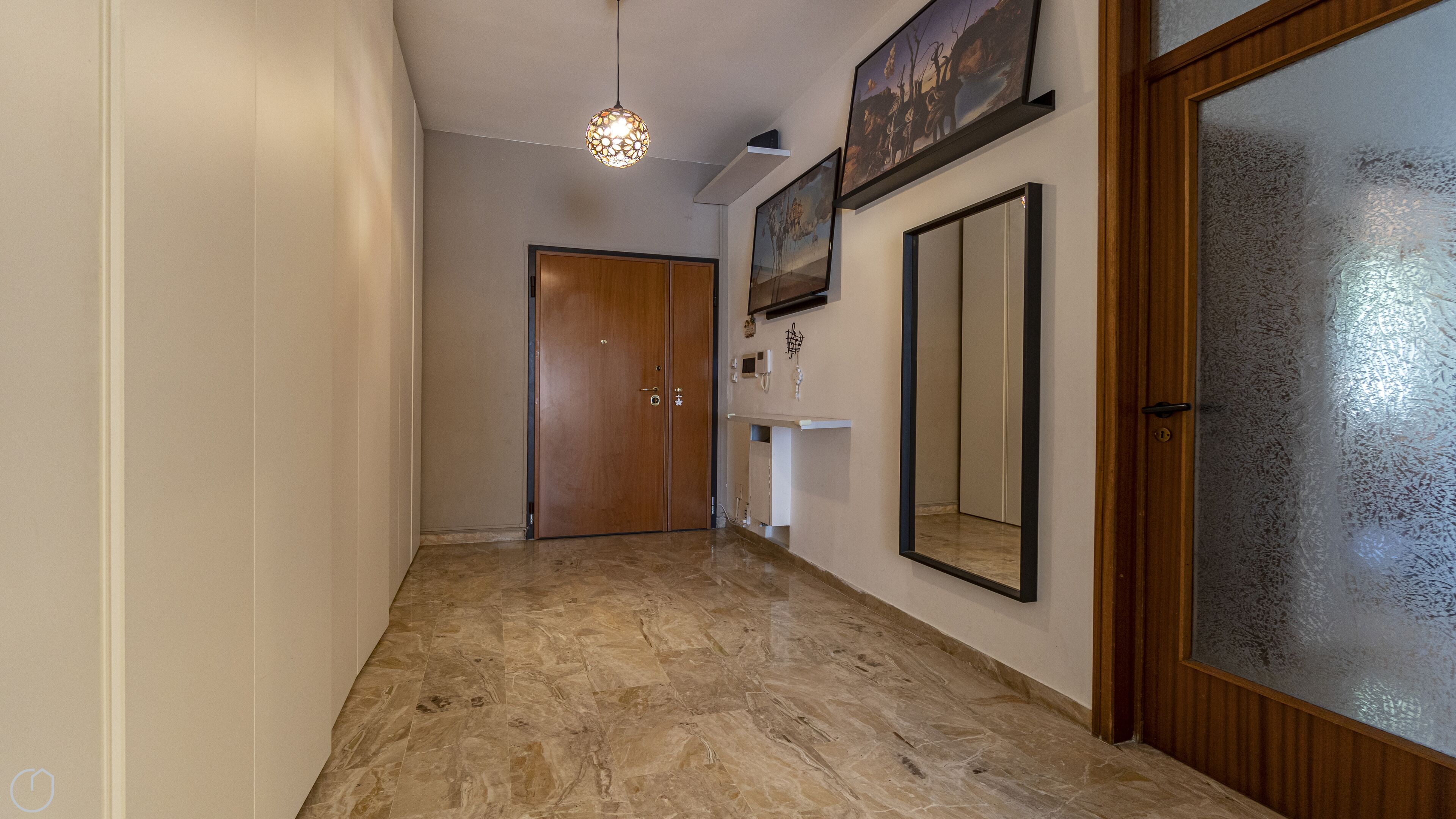 A hallway with a wooden door, a wall-mounted light fixture, and a mirror.