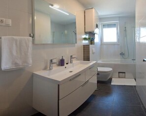 A modern bathroom with a white vanity, a large mirror, a bathtub, and a toilet. - Apartments Villa Diamond (Podstrana)