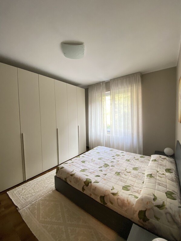 Un dormitorio con cama, armario, ventana con cortinas e iluminación en el techo.