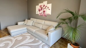 A living room with a sectional sofa, a decorative rug, a potted plant, and a wall-mounted artwork. - Sofia apartment near Bellagio (Lezzeno)