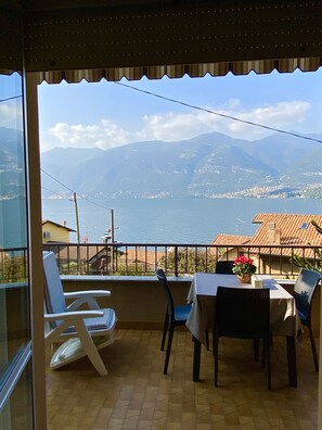 Un balcón con mesa y sillas, con vista a un paisaje montañoso y una masa de agua.