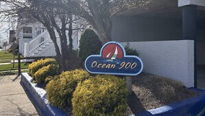 Schild für Ocean 900 mit einem Segelboot-Logo, umgeben von Büschen und einem blauen Rahmen.