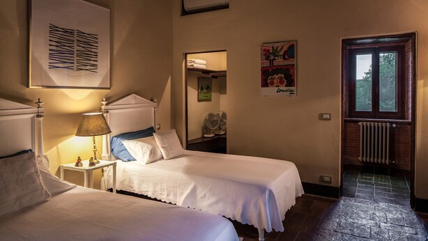 Une chambre avec deux lits, une lampe, un radiateur et une fenêtre donnant sur des arbres.