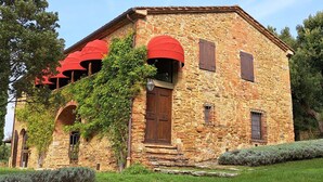 A stone building with a wooden door and red awnings, surrounded by greenery.