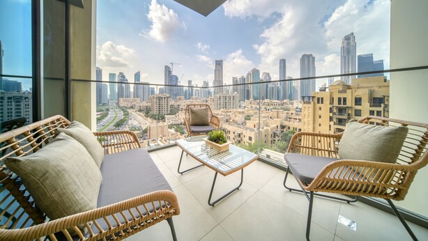 A balcony with wicker furniture, a glass table, and a city view.