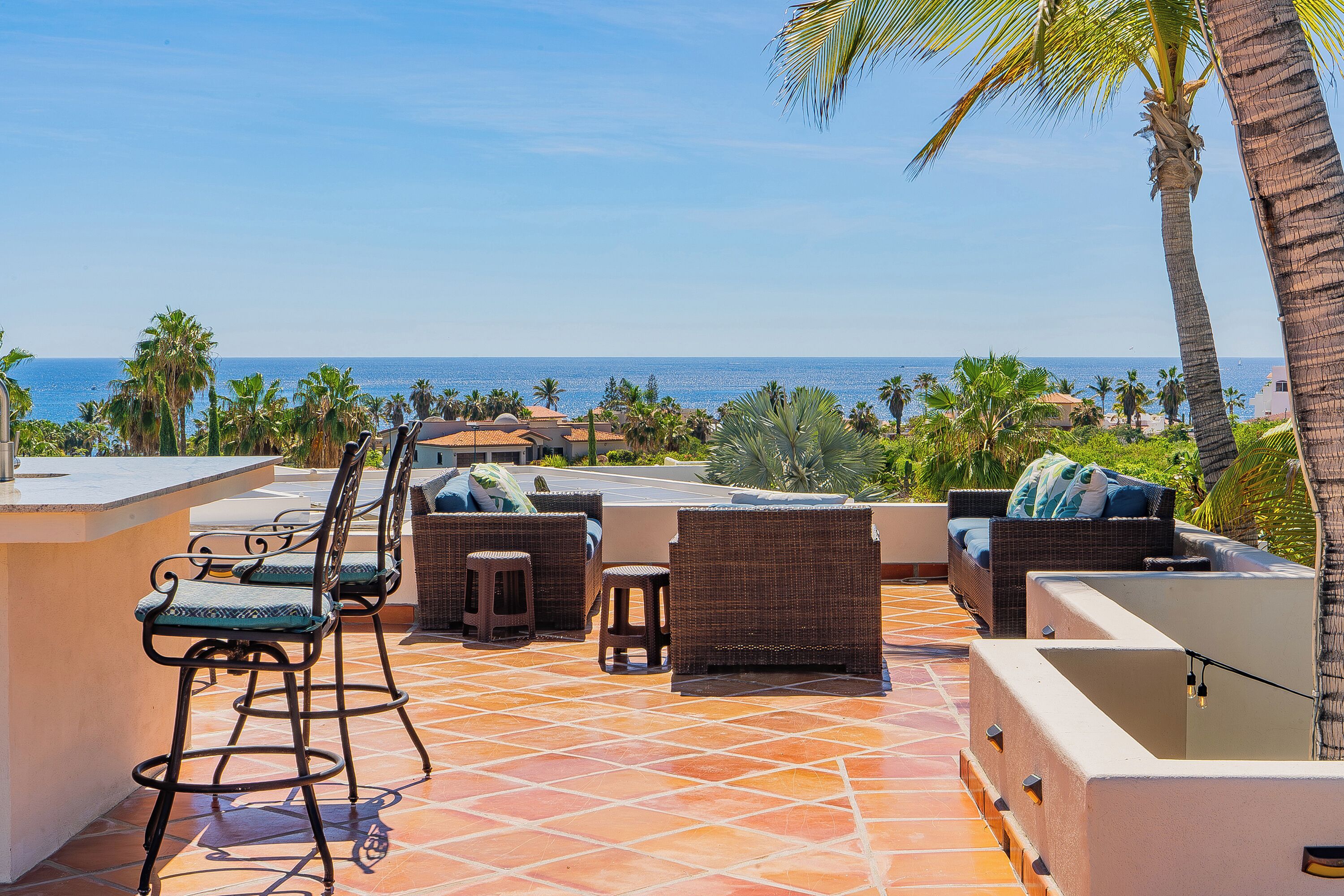 An outdoor patio with wicker furniture, a bar area, and a view of the ocean.