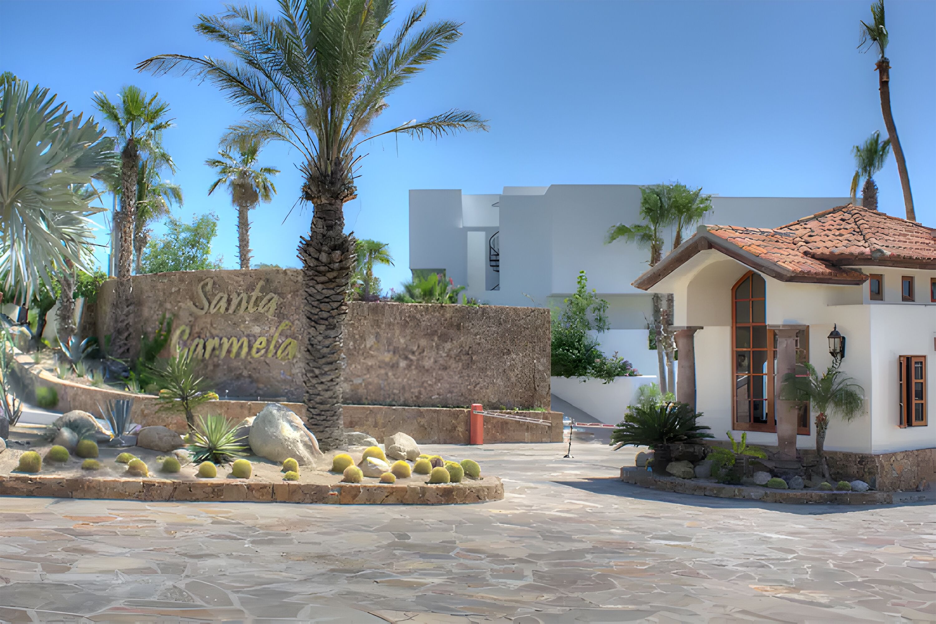 A building with a stone facade, palm trees, and a sign that reads "Santa Carmela."