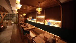 A restaurant with wooden tables and benches, decorative hanging lights, and a view of a desert landscape through the windows. - Hotel Layalee Grande Chennai (Chennai)