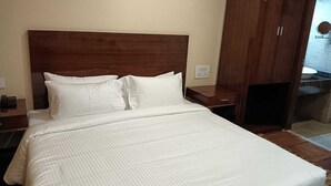 A hotel room with a large bed, wooden headboard, white bedding, a nightstand with a phone, and a wardrobe with a mirror. - Hotel Layalee Grande Chennai (Chennai)
