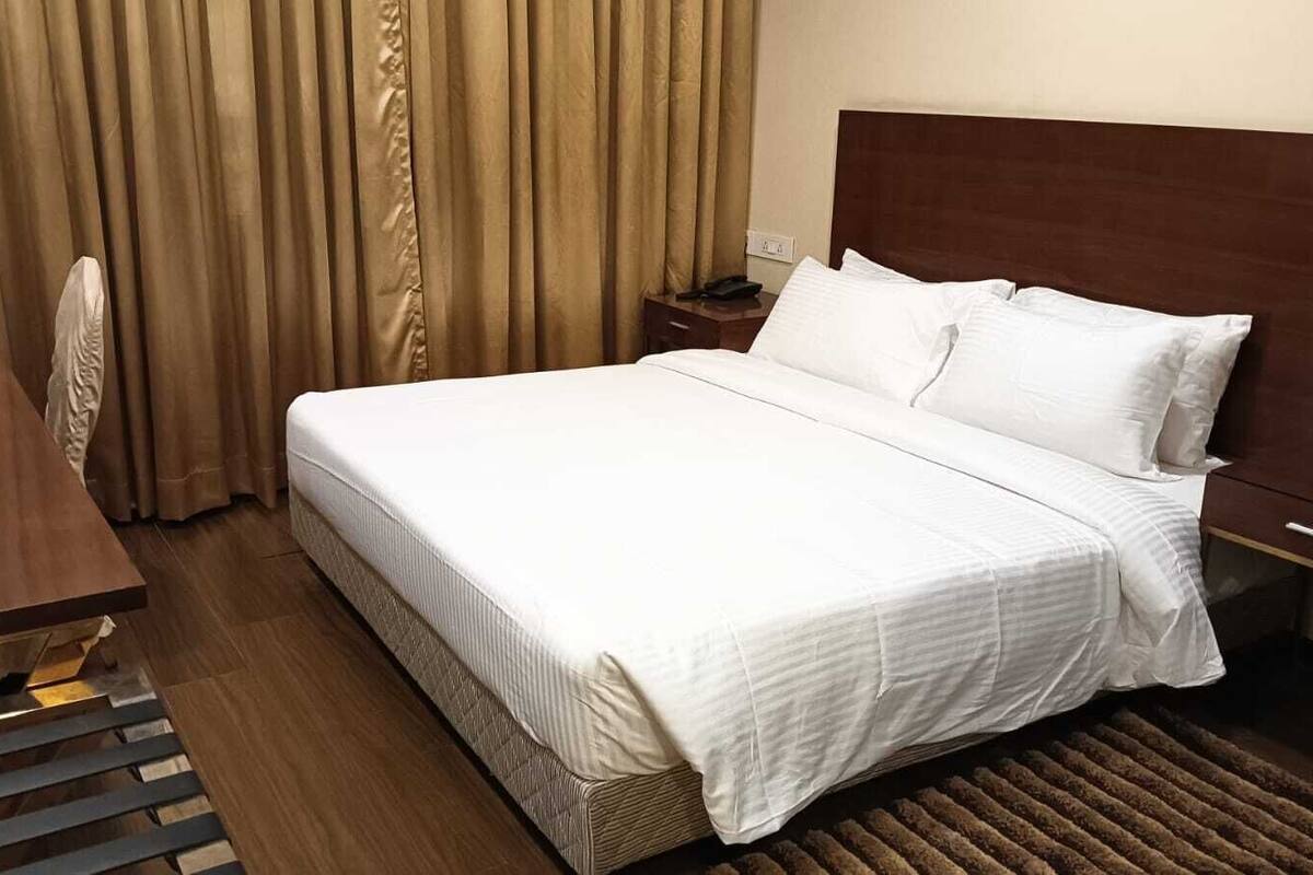 A hotel room with a large bed, a wooden nightstand, a chair, and a desk.