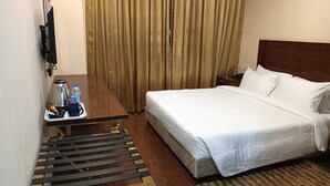 A hotel room with a bed, a bedside table with a tray of toiletries, a wooden floor, and a curtain. - Hotel Layalee Grande Chennai (Chennai)