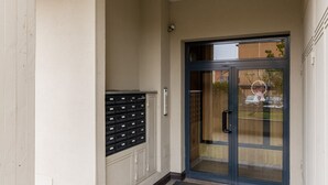 Une entrée d’immeuble avec une porte vitrée, une fente pour le courrier et un sol carrelé.