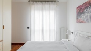 Une chambre avec un grand lit, un radiateur, une lampe blanche et un tableau représentant une cascade.