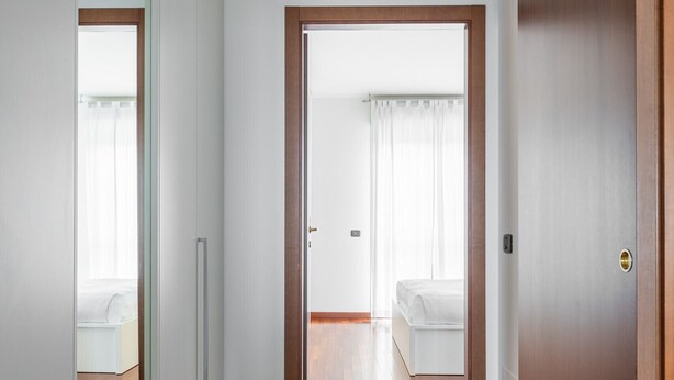 Un couloir au plancher de bois mène à une chambre à coucher qui contient un lit et une armoire blanche.