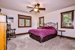 A bedroom with a bed, a ceiling fan, a chair, a small table, and windows with views of trees. - Stepaway Vacation Rentals-LCR#3 (St. Germain)