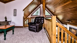 Una stanza accogliente con soffitto in legno, una poltrona in pelle, un tavolo in legno e vista attraverso ampie finestre.