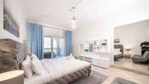A modern bedroom with a large bed, a chandelier, a TV, and a view of the city through the window. - Stylish Urban 1BR Gem in Fairmont-90AB2 (Dubai)
