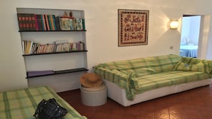 A living room with a green plaid sofa, a small round table with a hat, and shelves with books and decorative items.