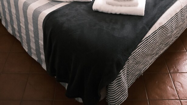Cama bem arrumada com roupa de cama listrada e duas toalhas dobradas.