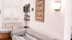 Quarto moderno com um sofá branco, uma janela com persianas, uma estante e um aplique de parede.