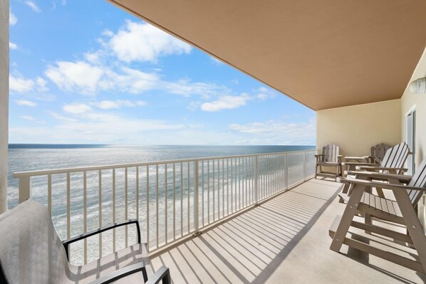 Un balcon avec vue sur l’océan, une balustrade et plusieurs fauteuils Adirondack.