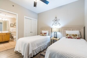Une chambre d’hôtel avec deux lits, une coiffeuse en bois, un miroir et un ventilateur de plafond.