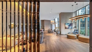 A spacious, modern interior with a wooden floor, a seating area with sofas and a coffee table, and a large window providing natural light. - CBD, Stylish, Heated Pool, Gym, Sauna, Steam, BBQ (Melbourne)