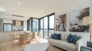A modern living room with a sofa, coffee table, and dining area. - Burleigh Seaside Sanctuary. Sea Views, Pool, Gym, BBQ Area, steps from beach. (Burleigh Heads)