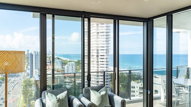 A modern room with large floor-to-ceiling windows offering a view of the ocean and cityscape. - Burleigh Seaside Sanctuary. Sea Views, Pool, Gym, BBQ Area, steps from beach. (Burleigh Heads)