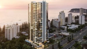 A modern high-rise building with multiple floors, surrounded by other residential buildings and a body of water in the background. - Burleigh Seaside Sanctuary. Sea Views, Pool, Gym, BBQ Area, steps from beach. (Burleigh Heads)
