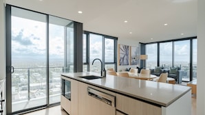 A modern kitchen with a large island, a built-in dishwasher, and a large window offering a city view. - Burleigh Seaside Sanctuary. Sea Views, Pool, Gym, BBQ Area, steps from beach. (Burleigh Heads)